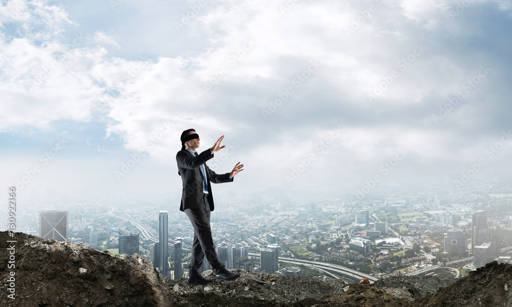 Young businessman in blindfold walking carefully and cityscape at background Young businessman in blindfold walking carefully and cityscape at background