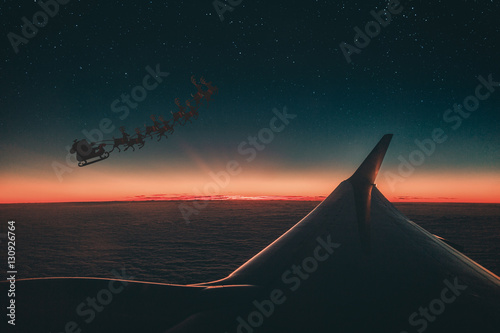 Slitta con Renne e babbo natale vista fuori dal finestrino di un aereo di linea al tramonto. photo