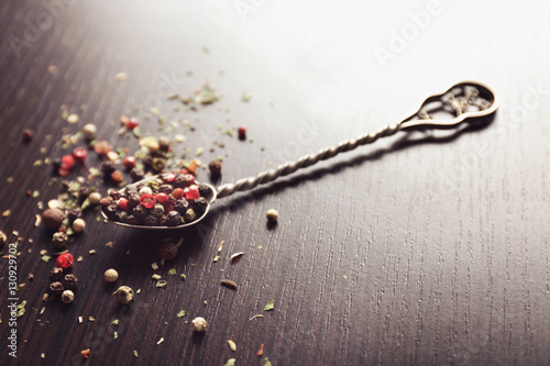 Spoon with assortment of pepper on wooden background