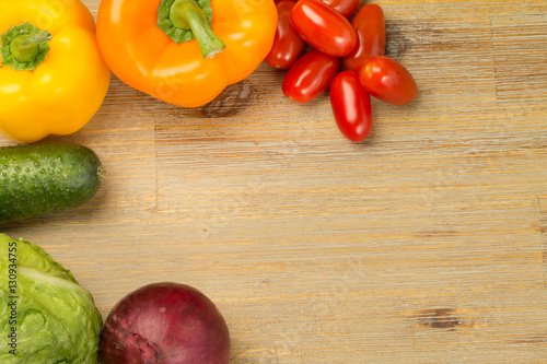 Vegetables on wooden table background around the sides. Cherry tomatoes, cucumbers, greens, cutting board, bell peppers orange and yellow, red onion. Vegan or vegetarian. Healthy eating. Salad.