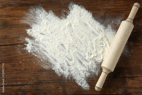 Rolling pin with flour on wooden background