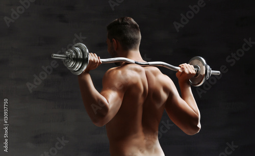 Sporty man doing exercises with barbell on dark background