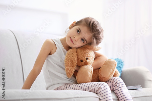 Funny little girl with cuddly toy sitting on sofa at home