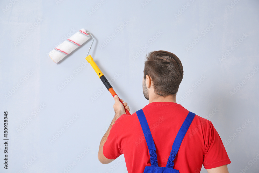 Young worker painting wall in room
