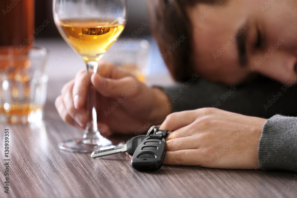 Drunk man sitting at table with car key and glass of alcoholic beverage, closeup. Don't drink and drive concept Drunk man sitting at table with car key and glass of alcoholic beverage, closeup. Don't drink and drive concept