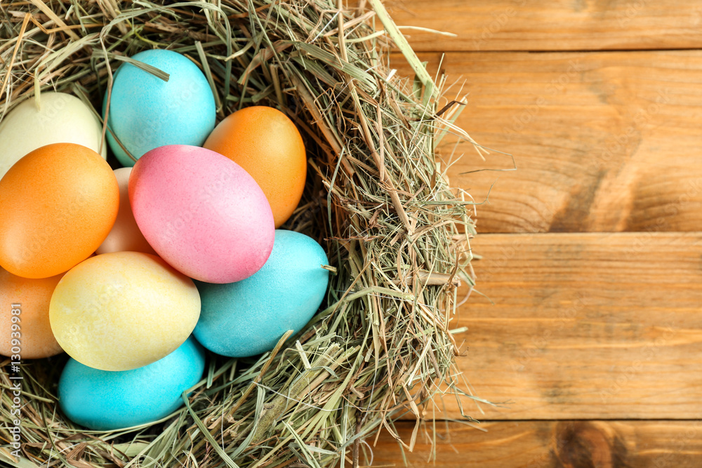 Fototapeta premium Nest with colorful Easter eggs on wooden table, closeup