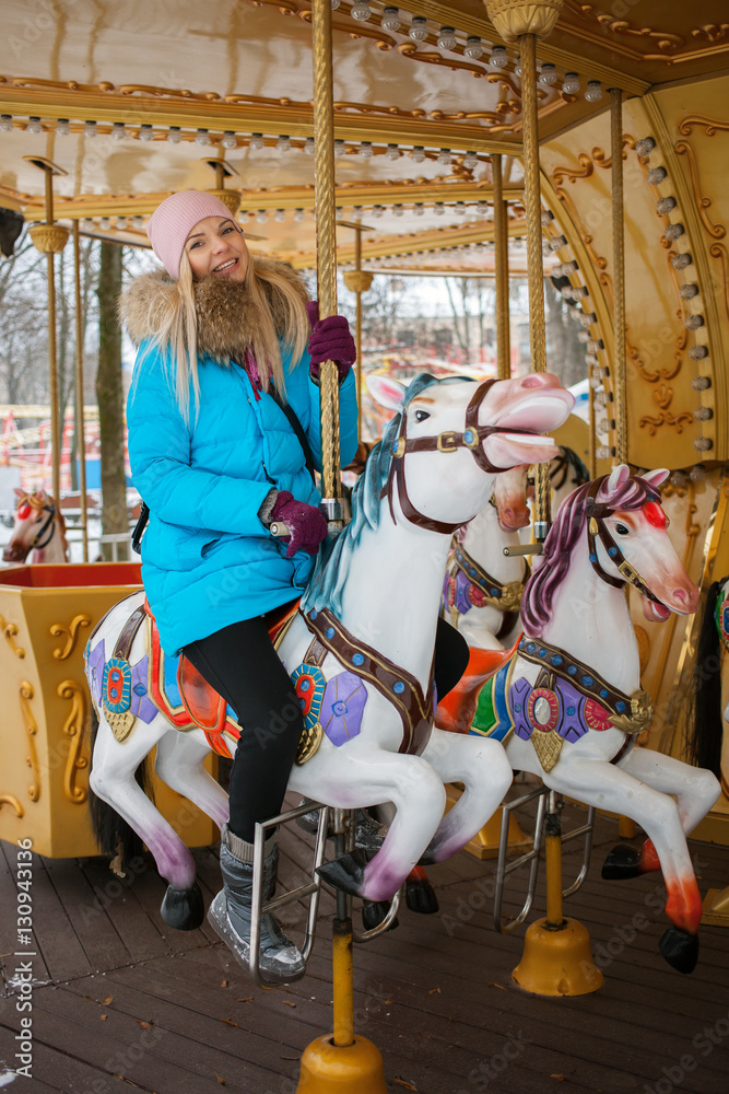 Young adorable blonde woman enjoys the winter holidays on the city park carousel. Winter active city lifestyle concept.
