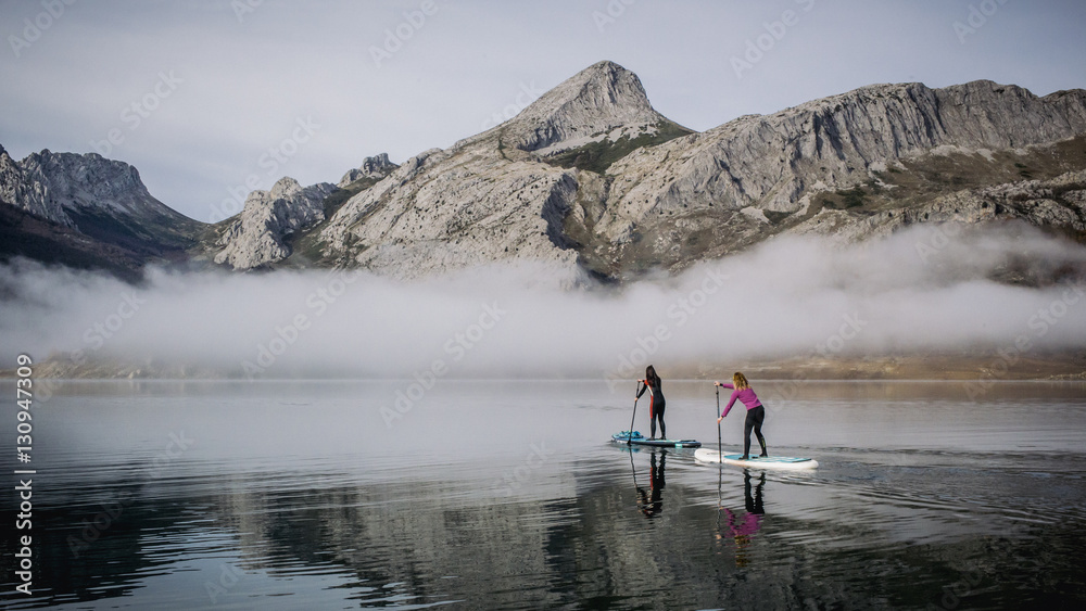 A group of people paddle surfing on a lake with fog and mountains
