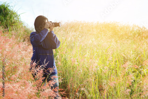 Photographer woman standing outdoor photography amidst the beautiful scenery of mountain and flowers grass amidst the warm sunshine. travel and natural Concept