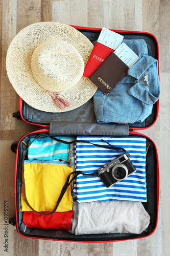 Open travel bag with clothes, film camera and passports on floor