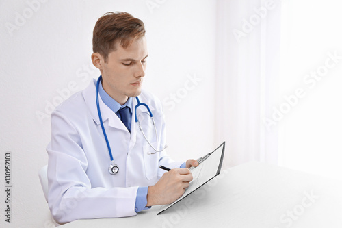 Handsome young doctor making notes while sitting at table