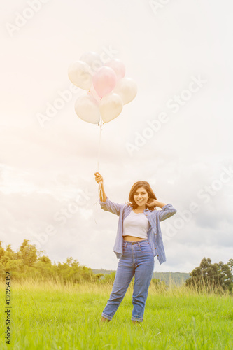Happy asin beautiful woman with colorful balloons in the grass field