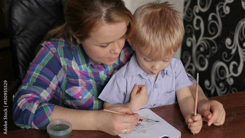 Young beautiful mother with son paint colors at home. Mom teaches son to paint colors. Young beautiful mother with son paint colors at home. Mom teaches son to paint colors.