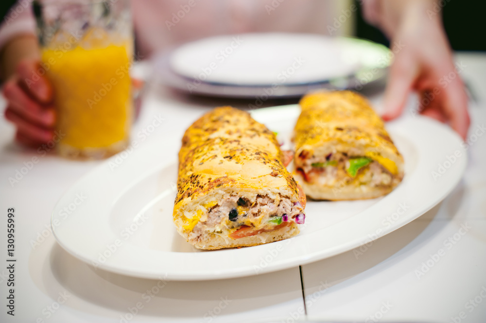 Pretty blonde woman in a pink shirt, eating at home. breakfast sandwich and peach juice. on white table in bright interior of kitchen in plate is sandwich juice poured in glass Pretty blonde woman in a pink shirt, eating at home. breakfast sandwich and peach juice. on white table in bright interior of kitchen in plate is sandwich juice poured in glass