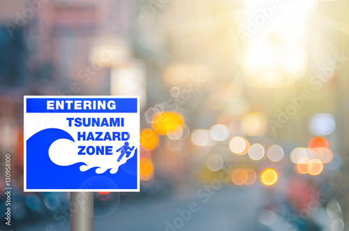 Tsunami hazard zone warning sign on blur traffic road with colorful bokeh light abstract background.