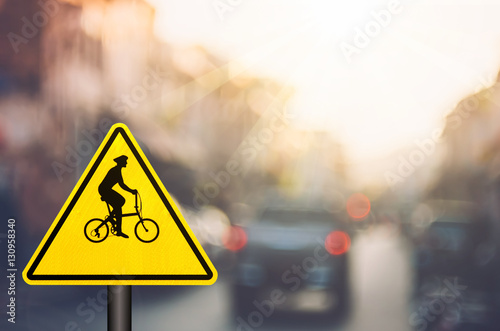 Bicycle warning sign on blur traffic road with colorful bokeh light abstract background.