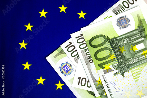 Hundred euro bills on european community flag. Golden stars circle. Angles of euro bills with hologram. Selective focus. Close up image. 