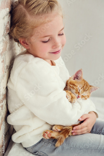 cute little girl holding hands on the ginger kitten