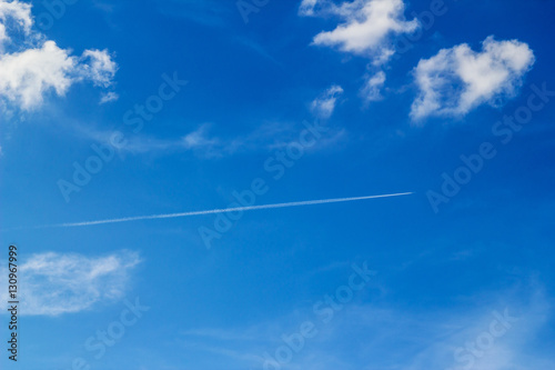 Plane leaving white lines against the blue sky and clouds..