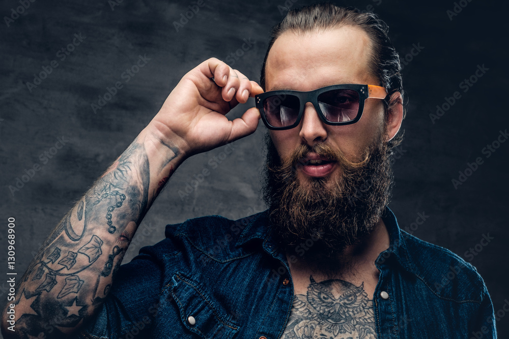Obraz premium Tattooed bearded man touches sunglasses on his face.