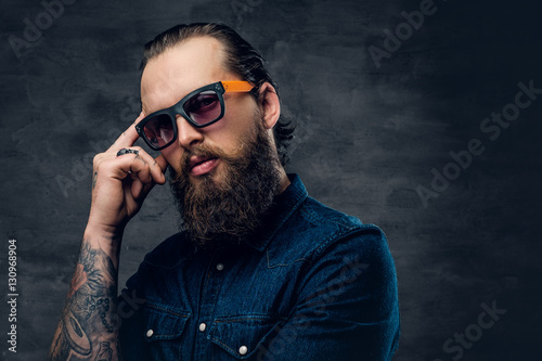 Thoughtful bearded male in sunglasses with tattoos on his arms.