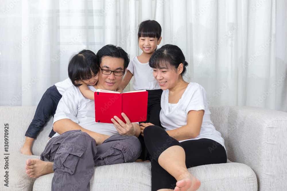 Happy Asian Chinese family reading book on the couch Happy Asian Chinese family reading book on the couch