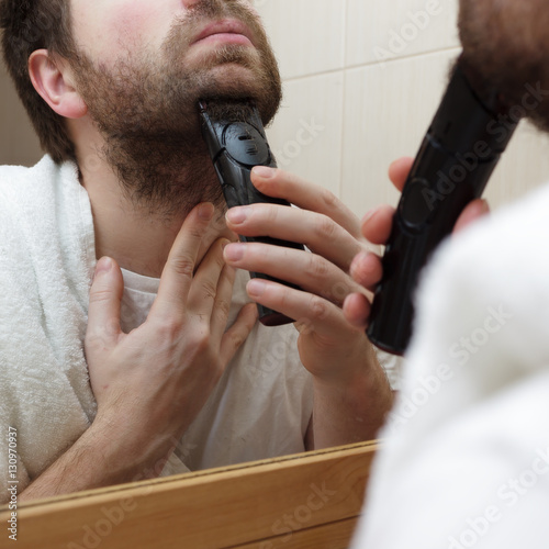 young man with a beard shave stubble with electric razor.