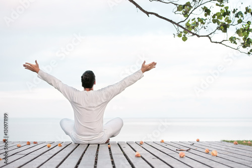 Man in white clothes meditating yoga on wooden pier