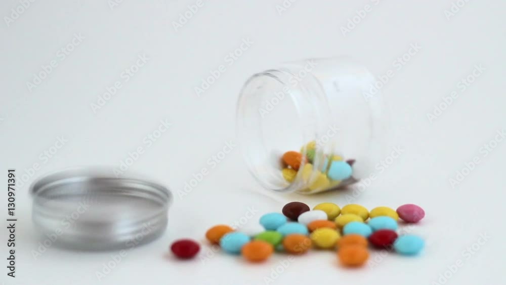 Colored smarties scattered out of an open glass jar, isolated on white background. Shallow depth of field. Colored smarties scattered out of an open glass jar, isolated on white background. Shallow depth of field.
