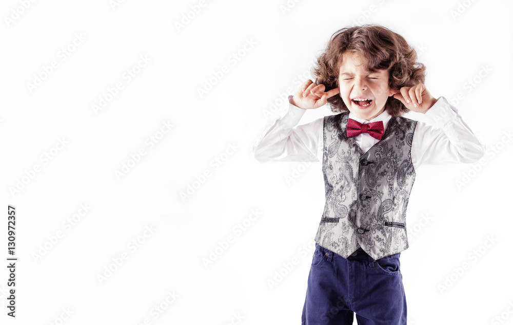 Curly cute boy in waistcoat and bow tie, his eyes shut, his fingers covering his ears and screaming. White background. Curly cute boy in waistcoat and bow tie, his eyes shut, his fingers covering his ears and screaming. White background.
