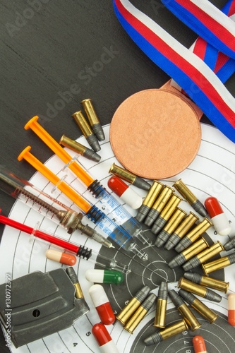 Syringe and medals. Doping in shooting sport. Abuse of anabolic steroids for sports. Deception in biathlon. The International Federation of biathlon - IBU. Ammunition and winners medals.
 photo