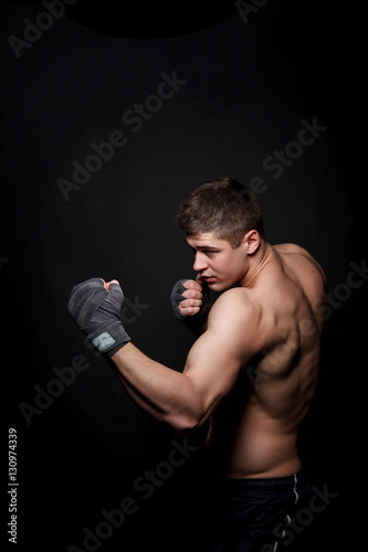 Muscular athletic man boxing on a black background. A man with a naked torso in shorts, hands peremotanye bandages for boxing. © nazarets