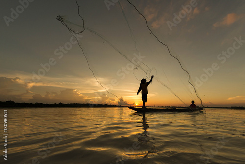 Silhouette of fisherman throwing net for fishing on the lake