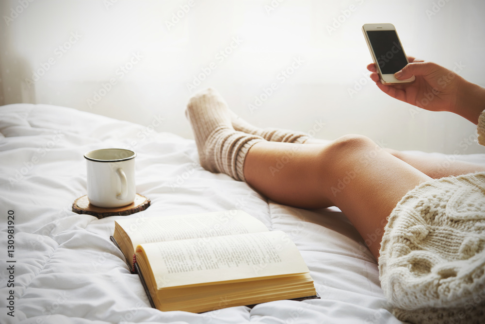 Soft photo of woman on the bed with old book, a cup of coffee and smart phone - obrazy, fototapety, plakaty 