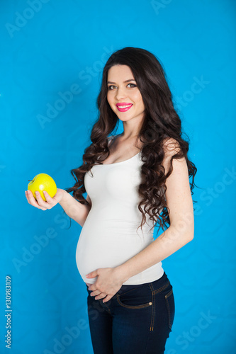 Pregnant happy young woman with green apple on blue background,