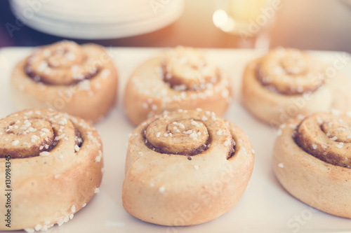 Cinnamon rolls on white plate. Sun and vintage effect applied.