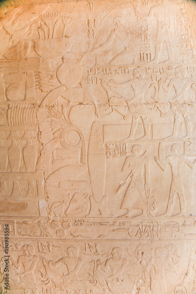 stone wall of egyptian temple with carved hieroglyphs, with ceremony procession of people with animals and food, in Egypt, Africa
