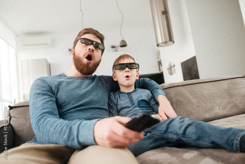 Shocked young father watching TV with his little cute son Shocked young father watching TV with his little cute son