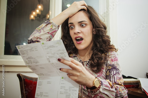 Foto Young woman shocked with the bills, can't believe the amount she has to pay