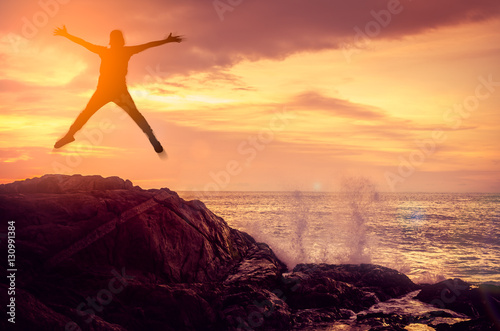 Feel good and freedom concept. Copy space of happy man jumping on rock sunset beach.