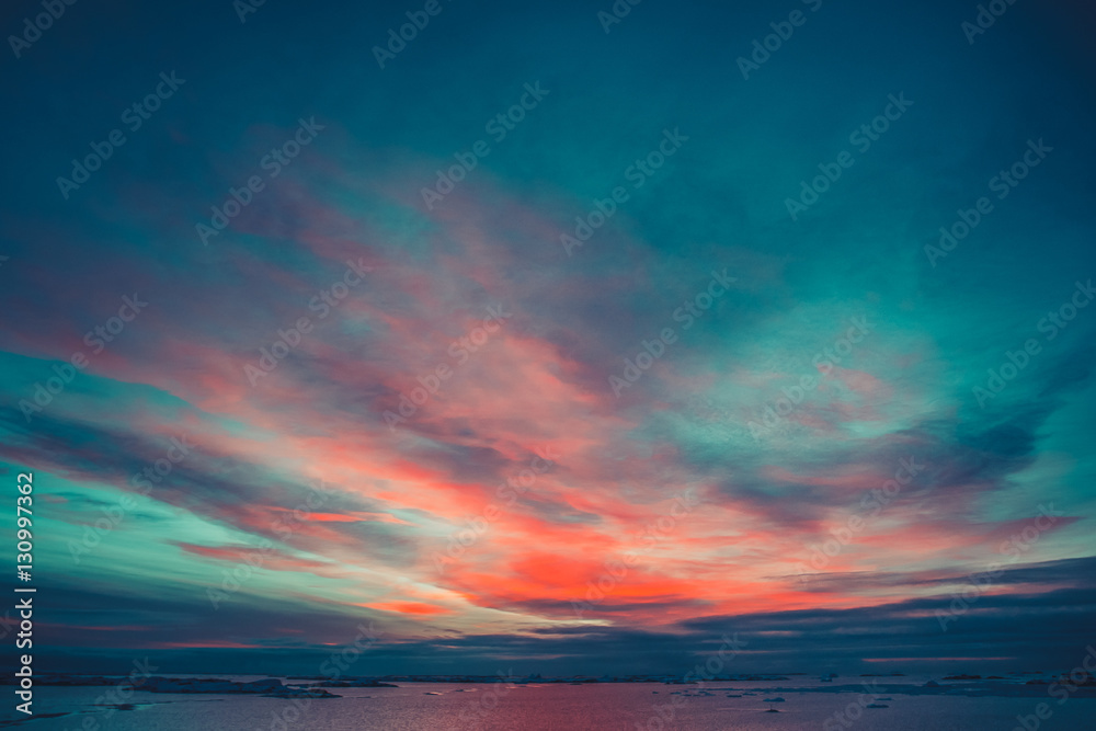 Summer sunset in Antarctica. Dramatic colourful cloudy sky above ocean and glaciers. Beautiful nature background
