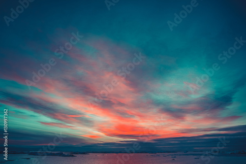 Summer sunset in Antarctica. Dramatic colourful cloudy sky above ocean and glaciers. Beautiful nature background
