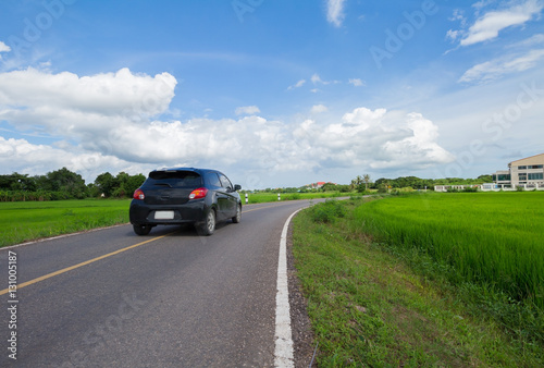 A black car on the road that pass trough green rice field