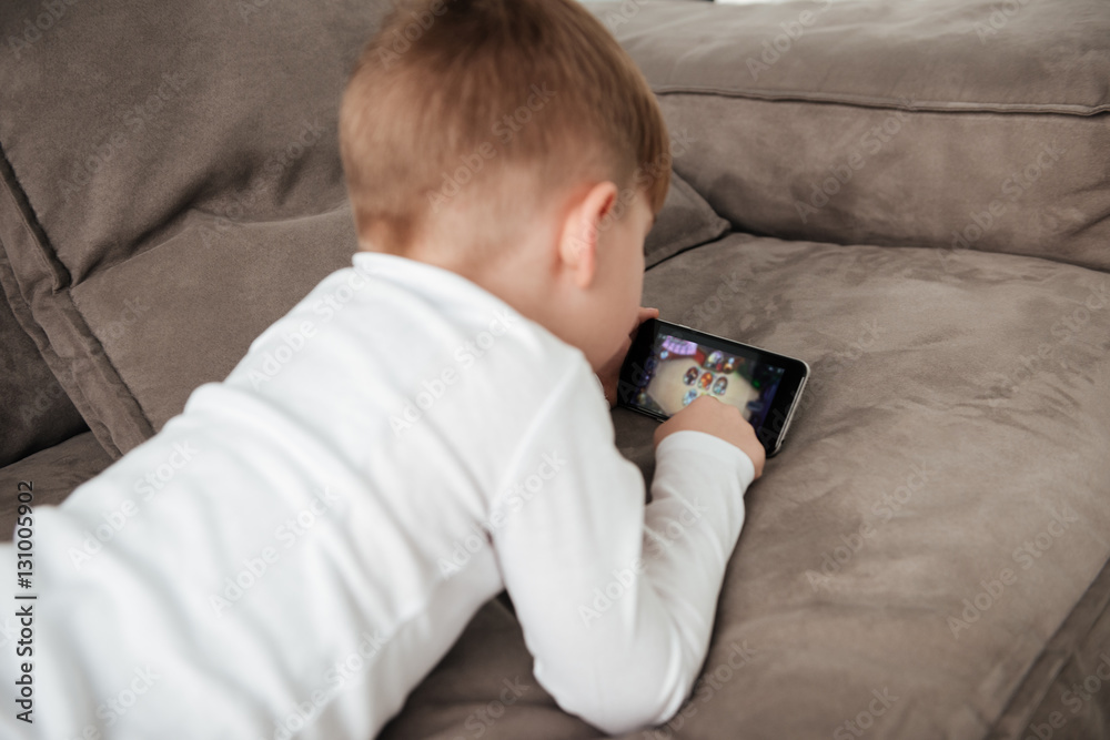 Obraz premium Little boy holding smartphone and playing game