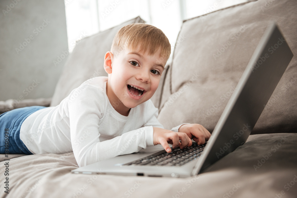 Happy boy using laptop computer while lies on sofa Happy boy using laptop computer while lies on sofa