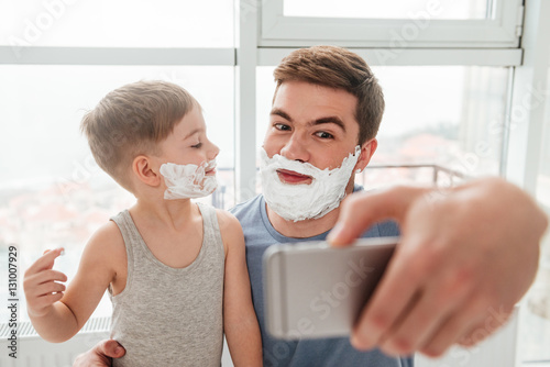Father and son applying shaving foam while taking selfie.