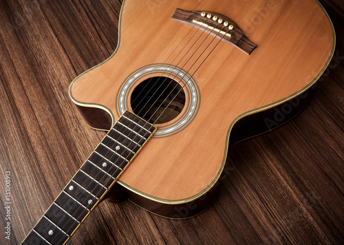 Acoustic guitar laid on wooden floor background.