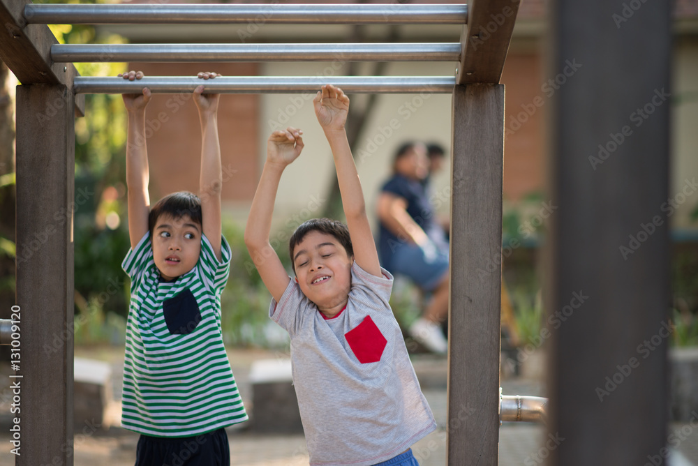 Fototapeta premium Little boy hanging on bar at playground