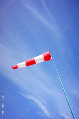Red and white windsock blows against a blue sky.