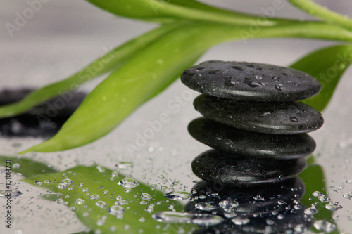 Spa concept. Volcanic rocks and bamboo on reflective background with raindrops. Relaxation, body care treatment, wellness